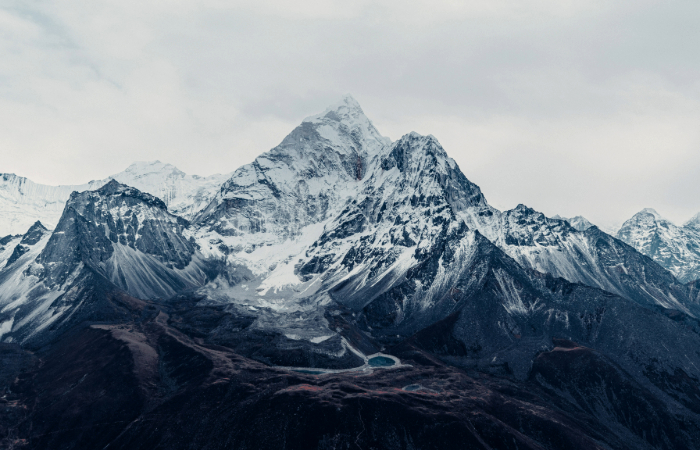 A panoramic view of the snow-covered summit of Mount Everest towering above the clouds, representing the majestic natural wonder that draws climbers.