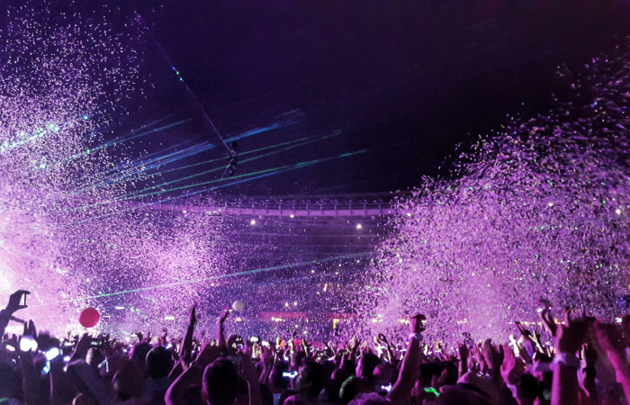 Excited fans at a Coldplay concert, waving colorful lights and singing along, capturing the vibrant energy of a live performance.